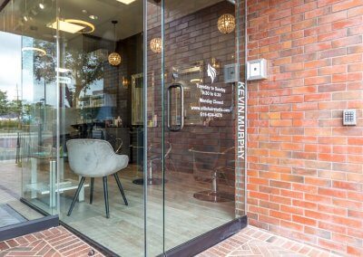 Chic entrance to the hair salon with a glass door, contemporary signage, and welcoming exterior design, reflecting a trendy and inviting atmosphere.